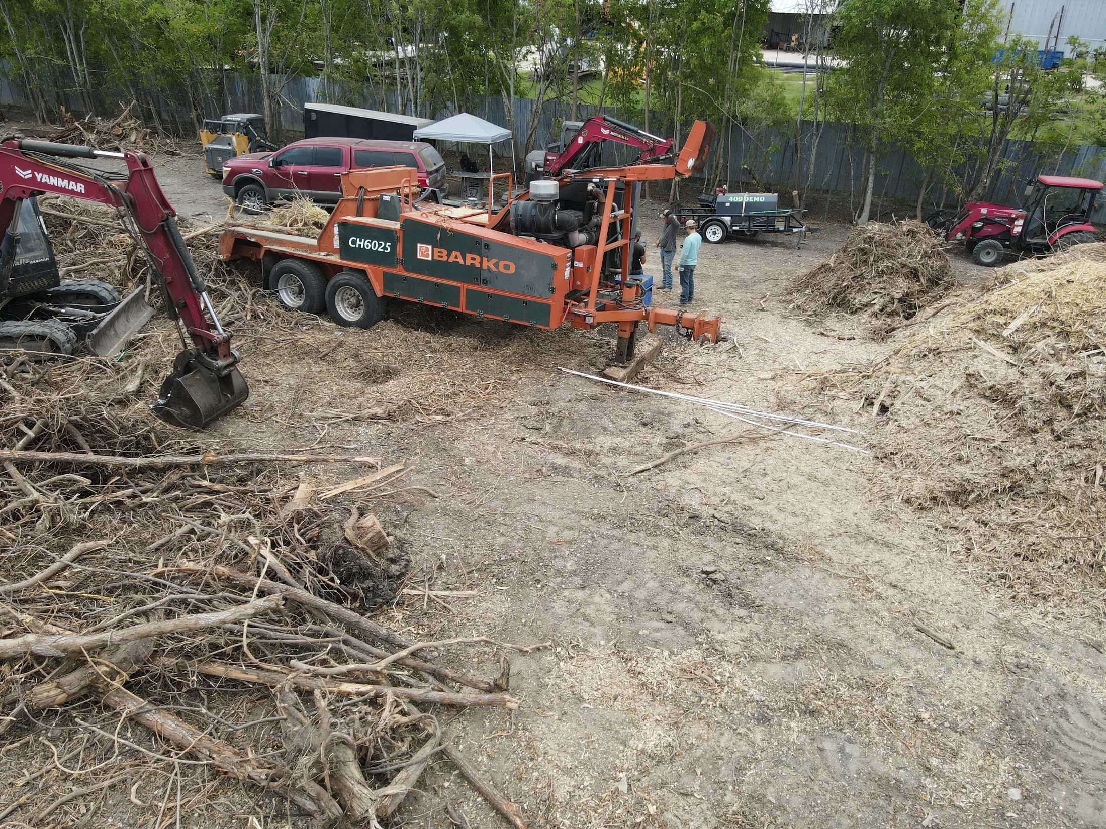 409 Demo whole-tree chipper beside an excavator and woody material on a clearing site
