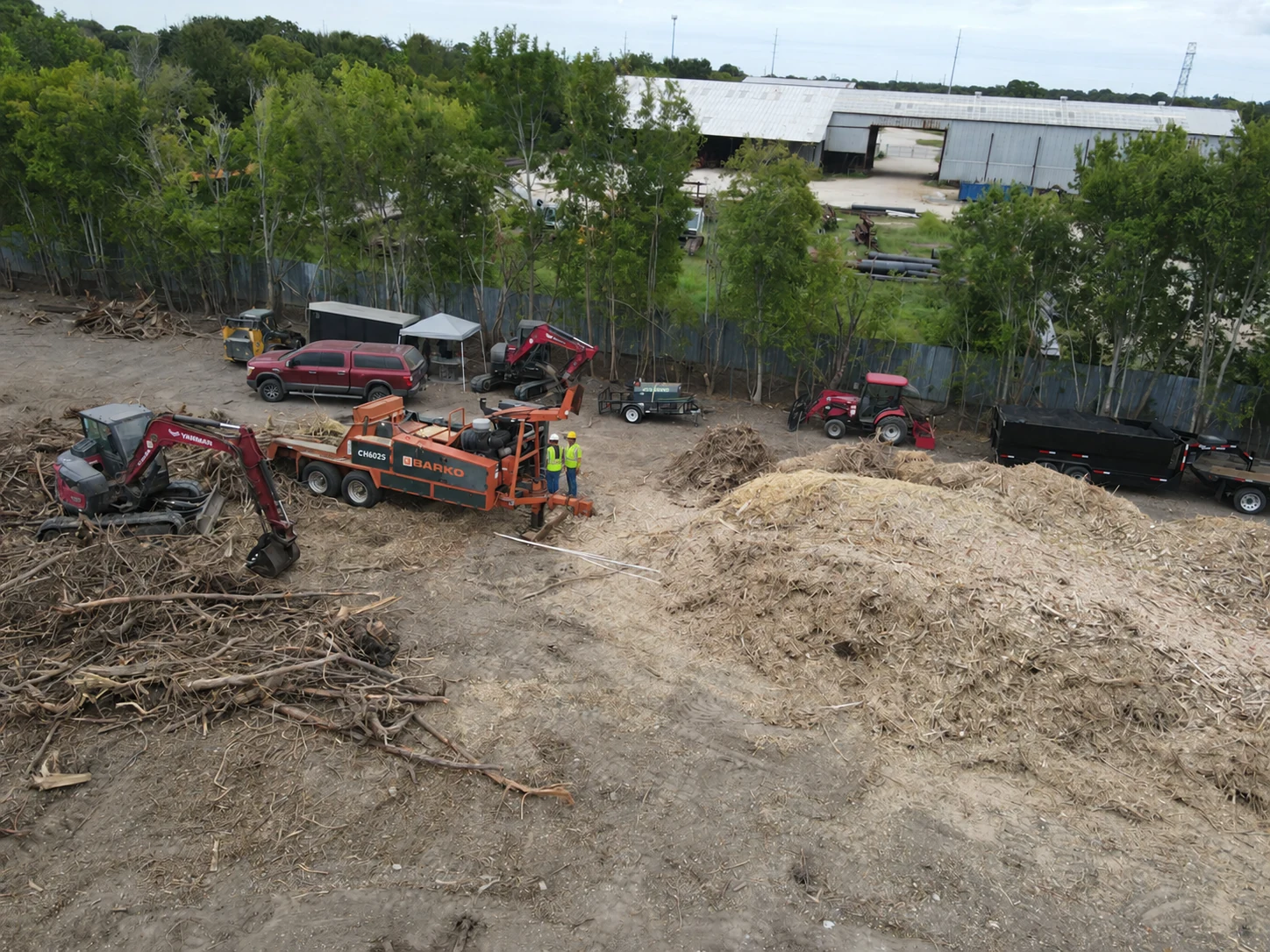 Whole-tree chipper and excavator beside a wood-chip pile on a land-clearing site