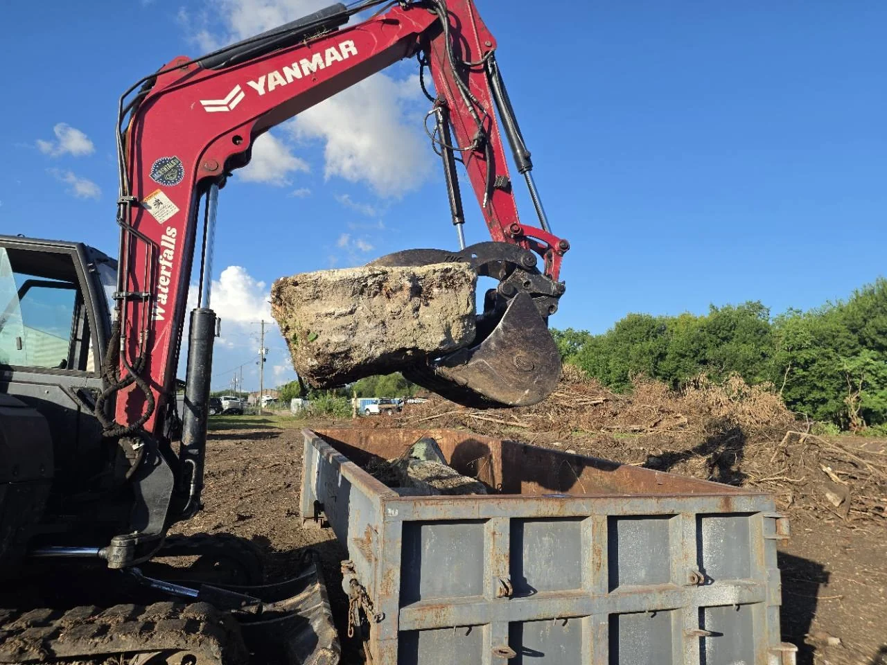 Excavator holding a substantial concrete section above a steel container