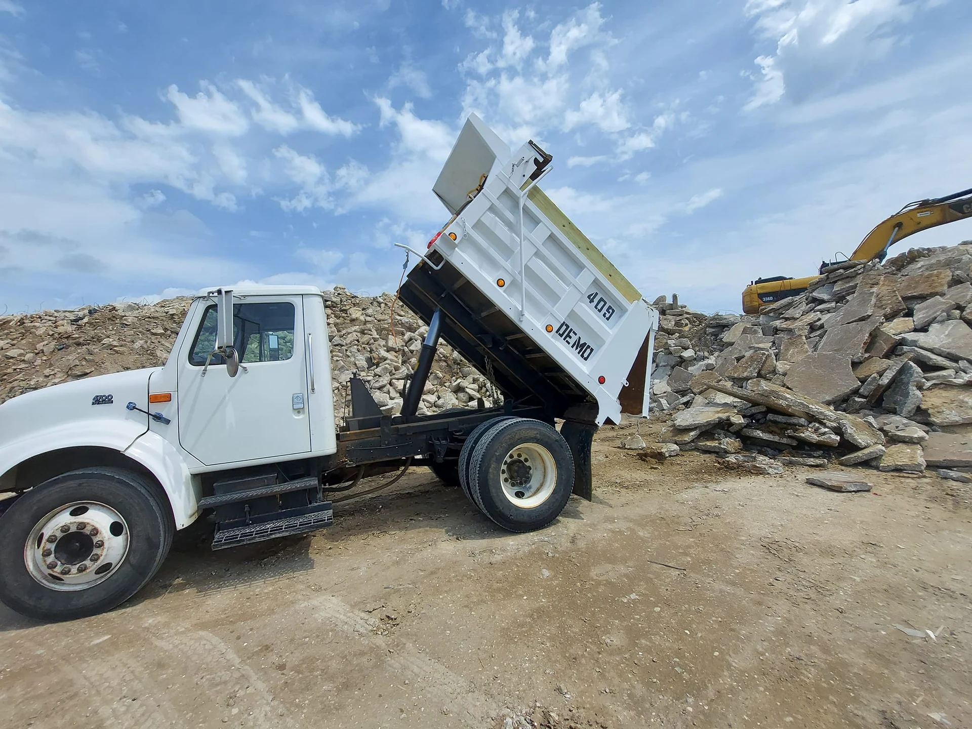 White 409 Demo dump truck with its bed raised beside piles of broken concrete