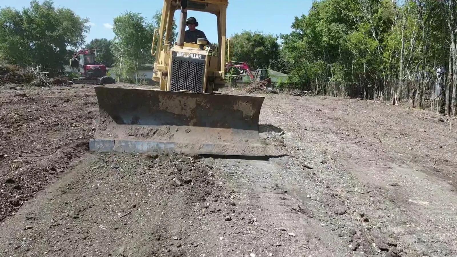 Tracked dozer shaping cleared ground with excavators working in the background