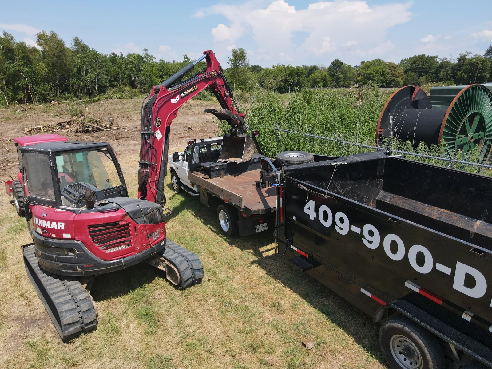 Red excavator beside a work truck and a 409 Demo trailer