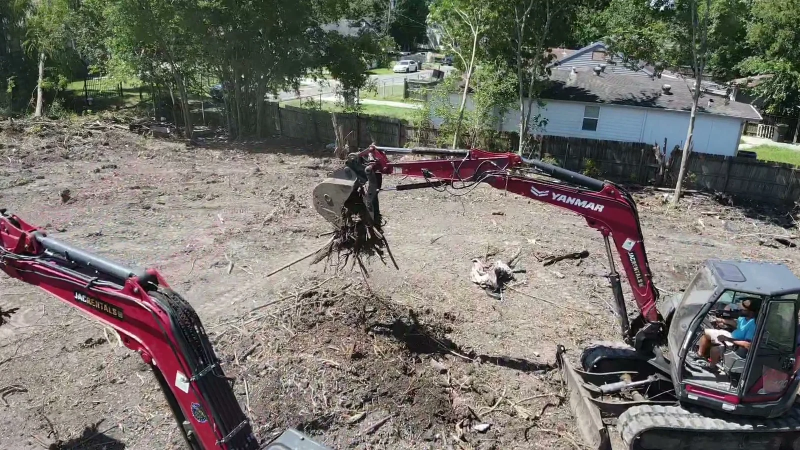 Excavator lifting a root mass and woody debris from cleared ground