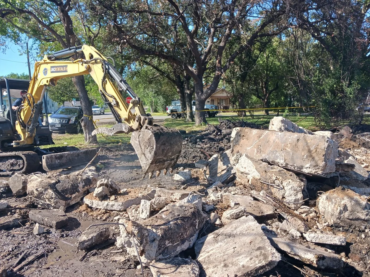 Excavator bucket beside broken concrete slabs and exposed reinforcing steel